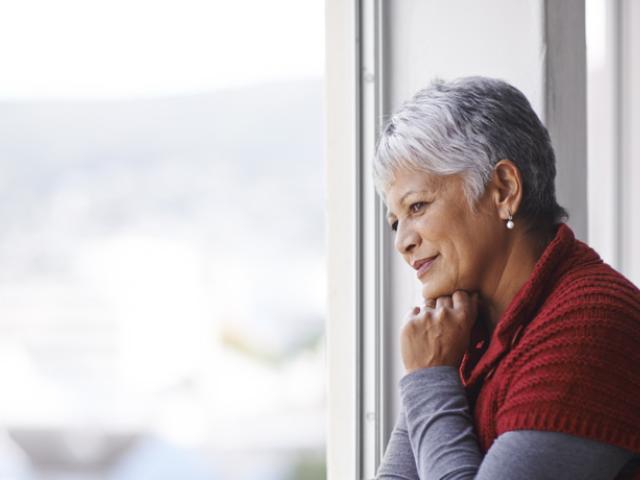 Mujer mayor en Ecuador mirando por la ventana en actitud reflexiva tras recibir un diagnóstico de Parkinson.