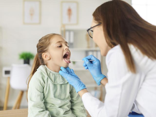 Doctora examinando si niña tiene pus en la garganta.