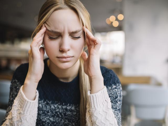 Mujer joven con migraña intensa sosteniendo su cabeza por el dolor.